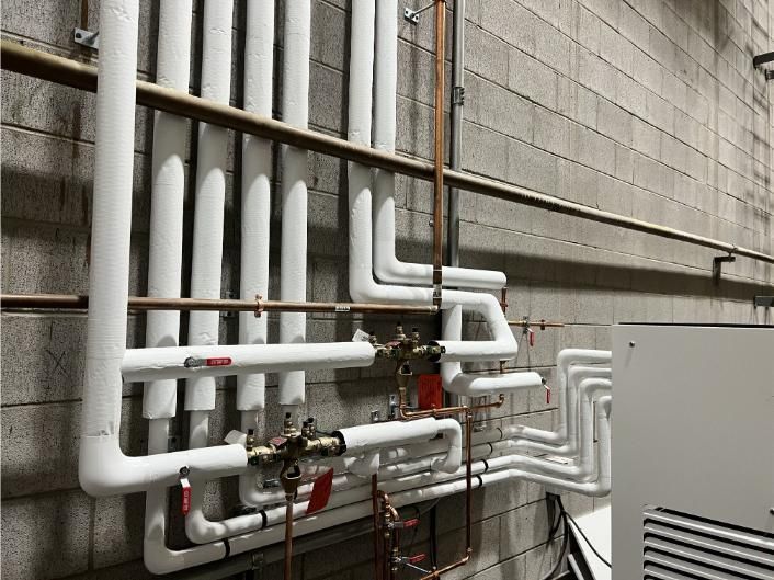 Pipes with white insulation on a gray cinder block wall, with copper piping and a metal box.