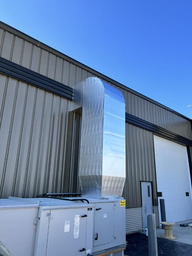 Metal ductwork on a building exterior, connected to HVAC unit. Bright blue sky background.