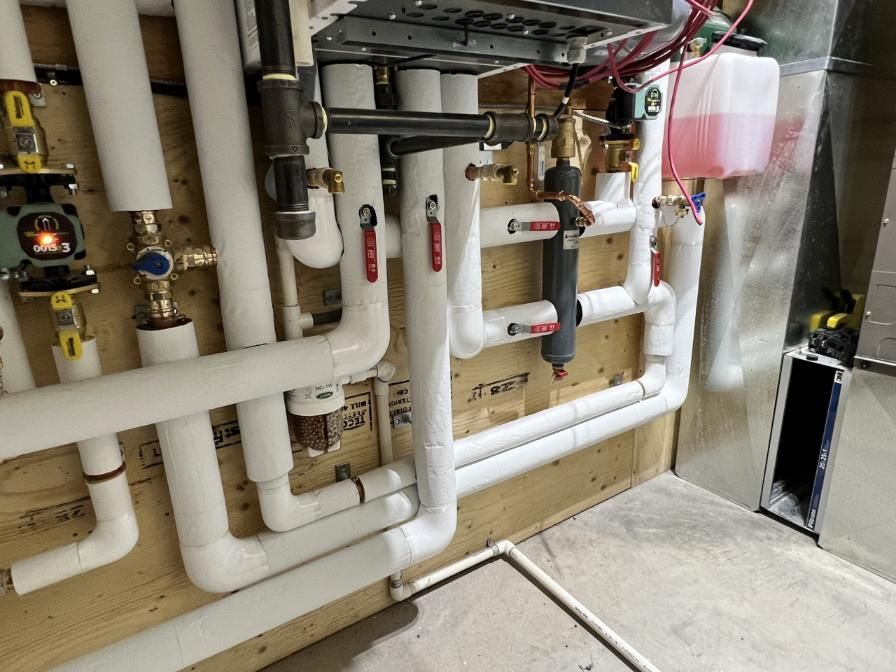 White pipes and valves of a heating system on a wooden wall.  Red, pink, and gold accents.