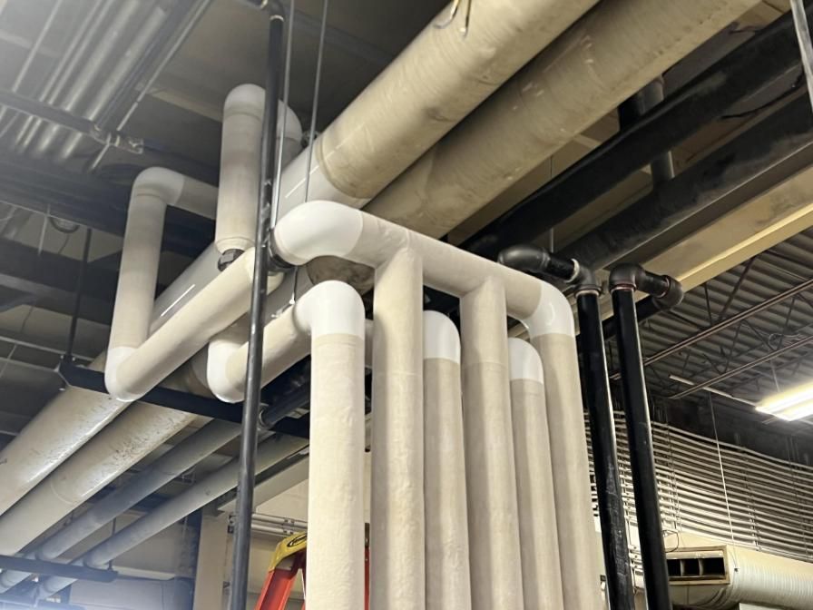 Pipes insulated with beige material, attached to ceiling, some curved.
