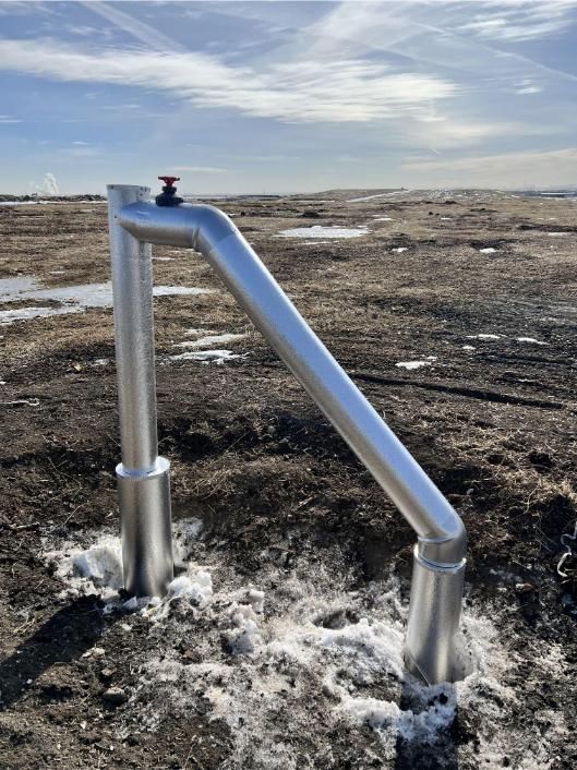 Silver industrial pipe structure with a red valve, set in a muddy, snow-covered landscape.