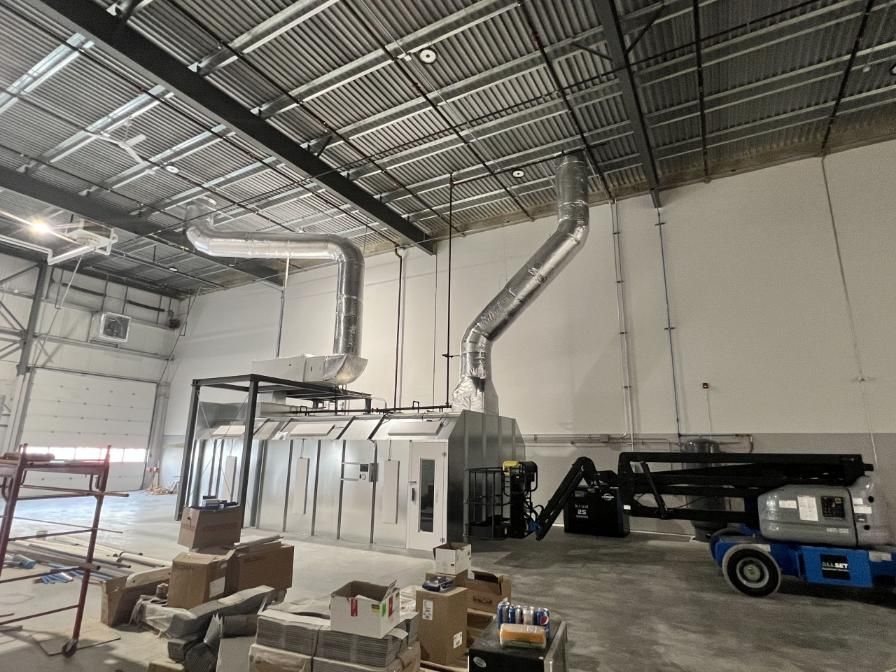 A large, unfinished industrial space with a paint booth and ventilation system.