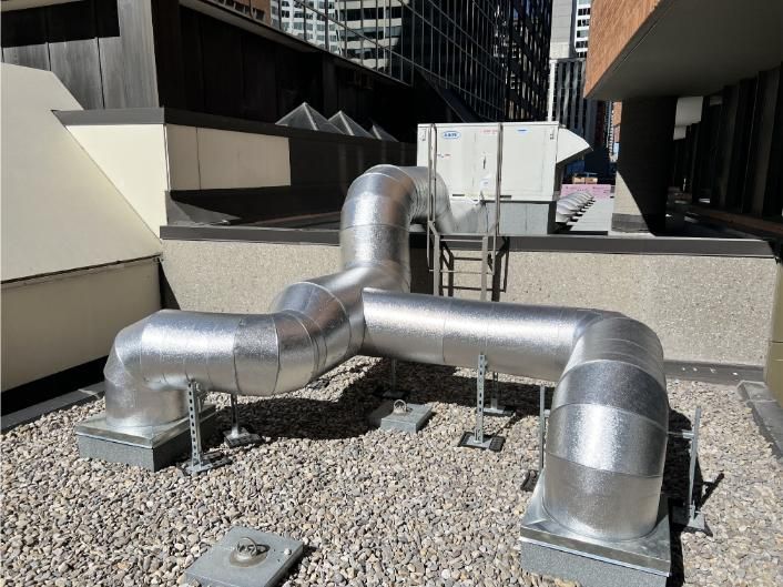 Silver insulated HVAC ductwork on a building rooftop with an air conditioning unit.