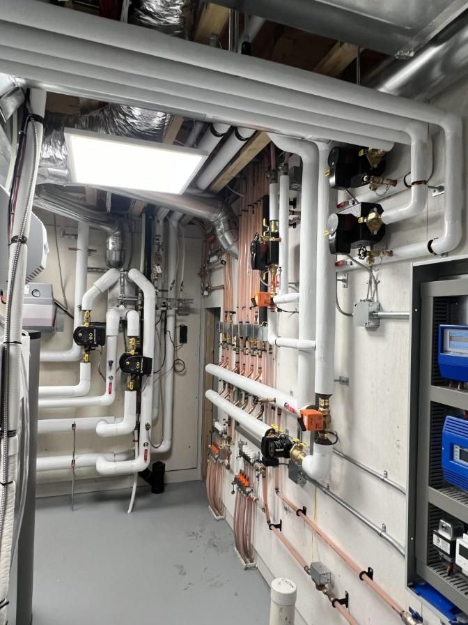 Mechanical room with white pipes, valves, and equipment.