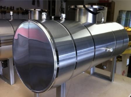 Stainless steel industrial tanks on metal stands in a workshop setting.
