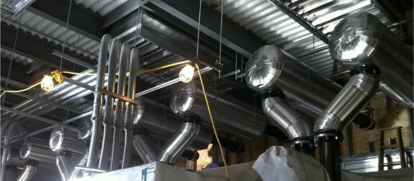Metal ventilation system under construction, with pipes and ductwork. Industrial setting with lighting.