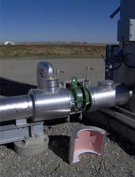 Industrial pipe with insulation removed, showing a green valve and metal components outdoors.