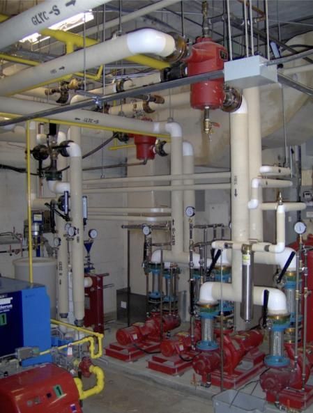 Mechanical room with pipes, red pumps, and tanks.