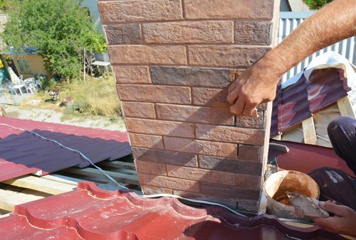A man is working on a brick chimney on a roof.