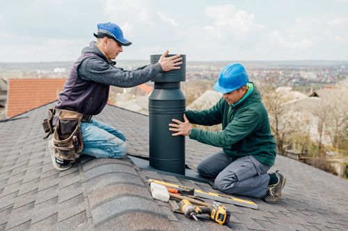 Two men are working on a chimney on the roof of a house.