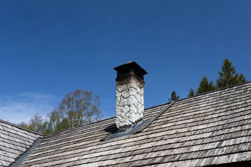A chimney on top of a wooden roof with a blue sky in the background.