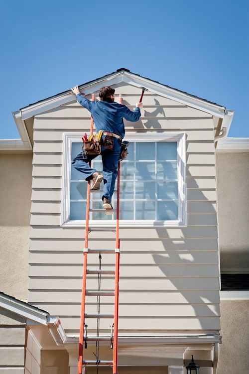 A man on a ladder is working on the side of a house.