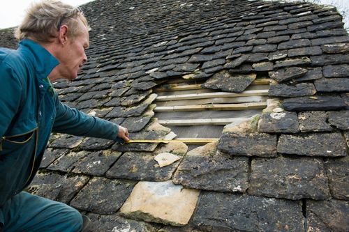 A man is measuring a roof with a tape measure.
