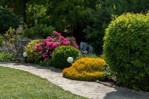 A stone walkway in a garden surrounded by bushes and flowers.