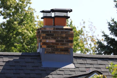 A brick chimney on top of a roof with trees in the background.
