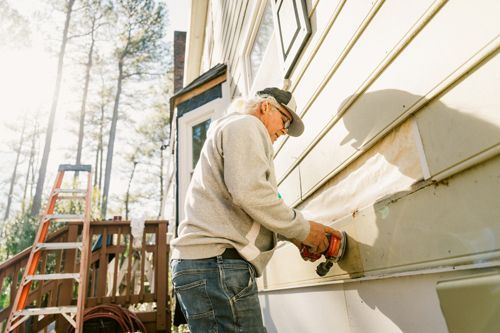 A man is working on the side of a house with a drill.