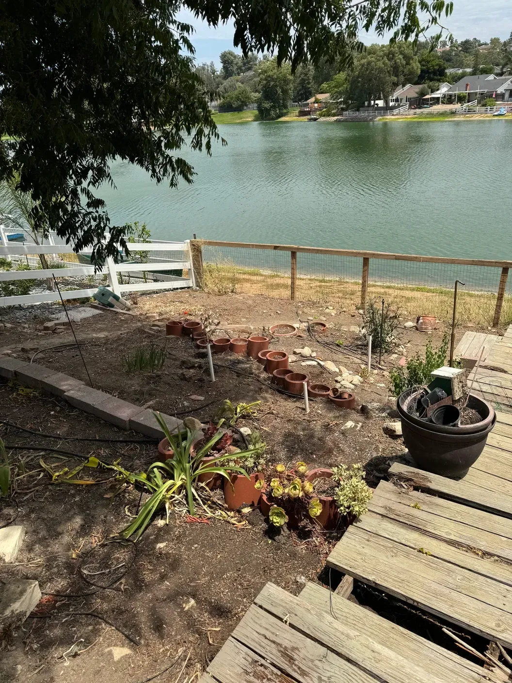 A wooden deck overlooking a lake with potted plants and a fence.