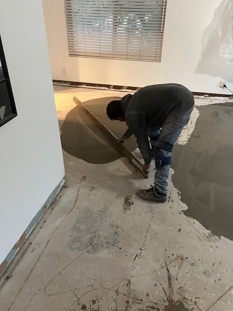A man is laying concrete on the floor in a room