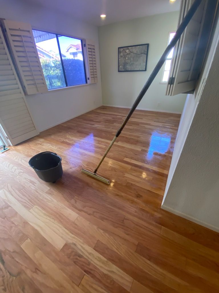 A mop is sitting on a wooden floor next to a bucket.