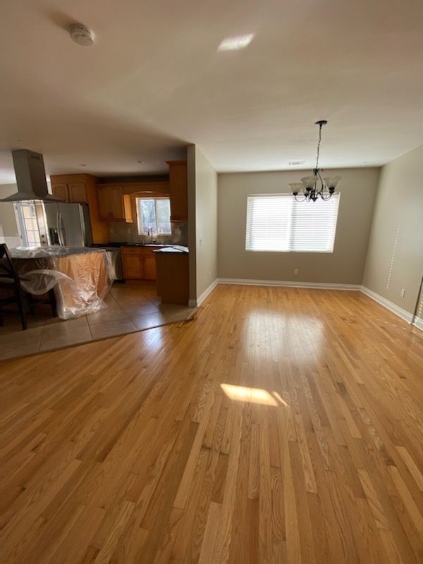 A living room with hardwood floors and a kitchen in the background.