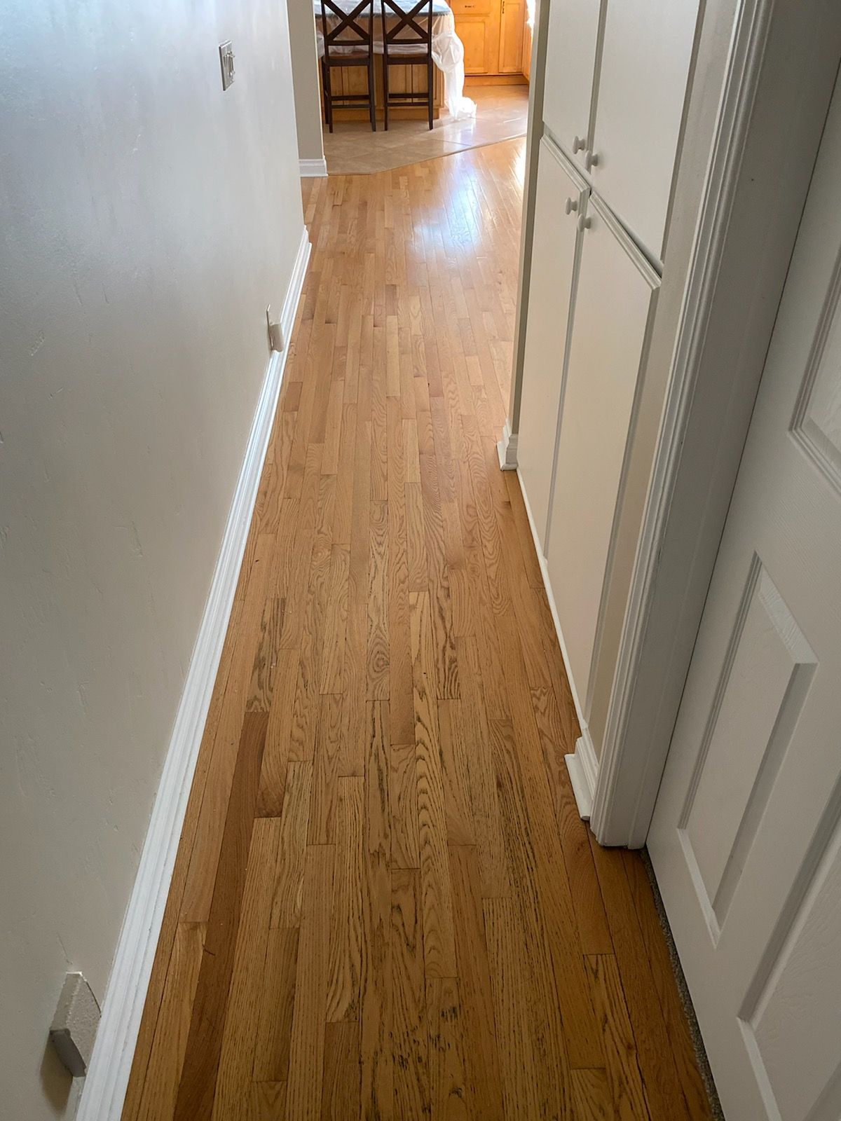 A hallway with hardwood floors and white cabinets in a house.