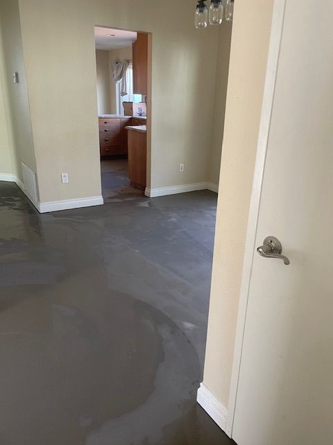 A room with a gray floor and a white door leading to a kitchen.