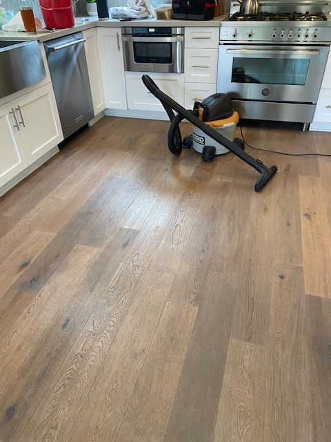 A vacuum cleaner is sitting on a wooden floor in a kitchen.