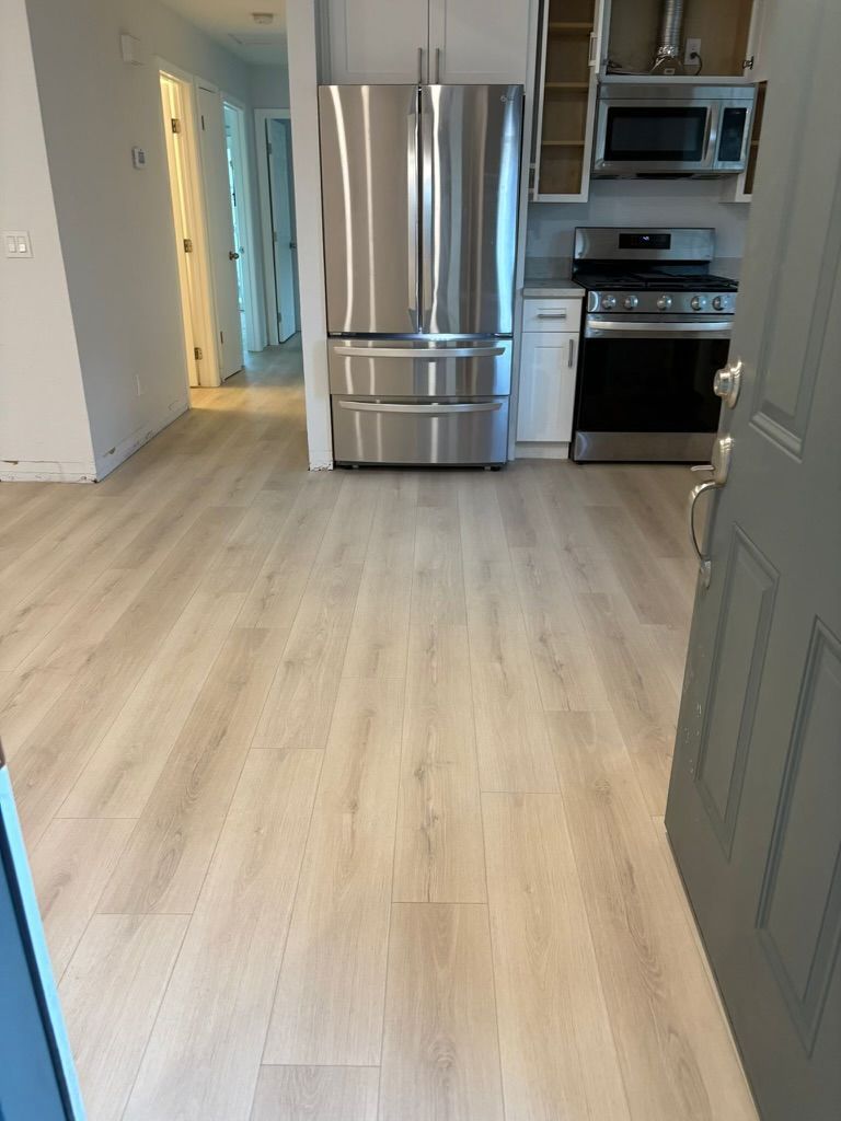 A kitchen with a stainless steel refrigerator and stove with laminate flooring