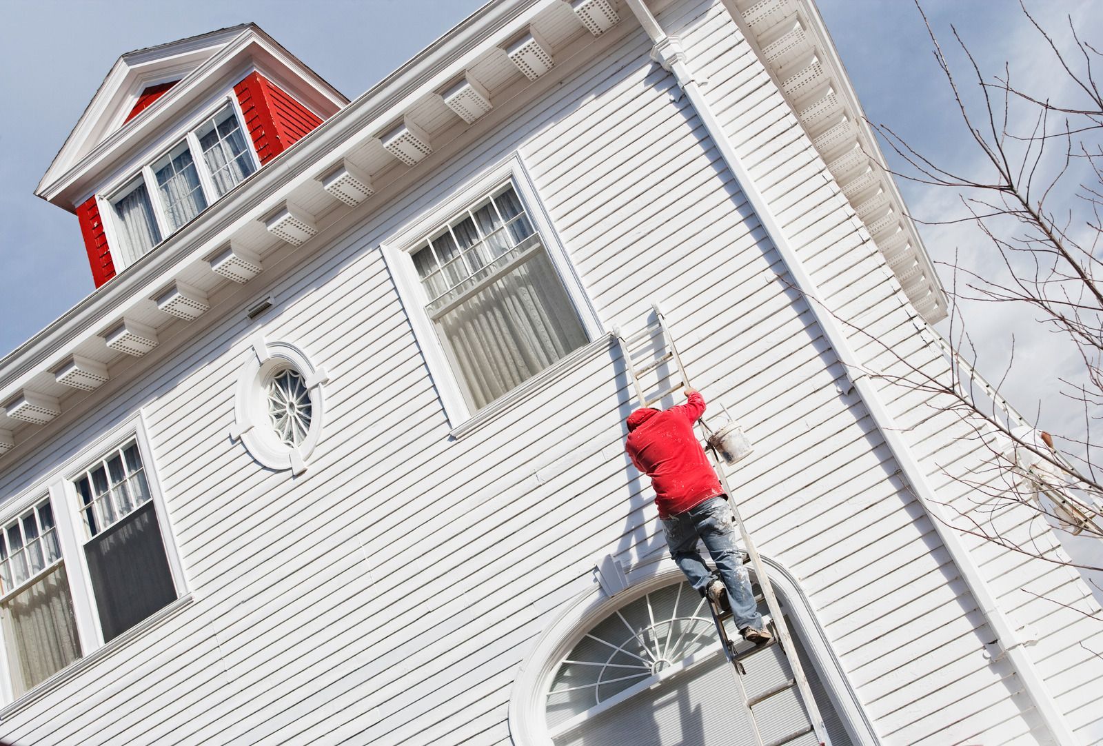 Person in red jacket climbing a ladder up a white house with red trim.