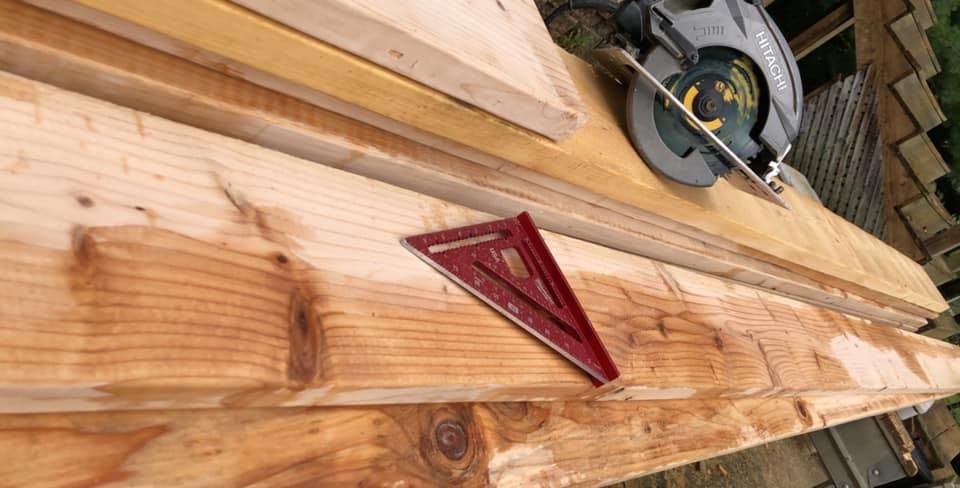 A red square is placed on a wooden beam next to a circular saw; outdoor setting.