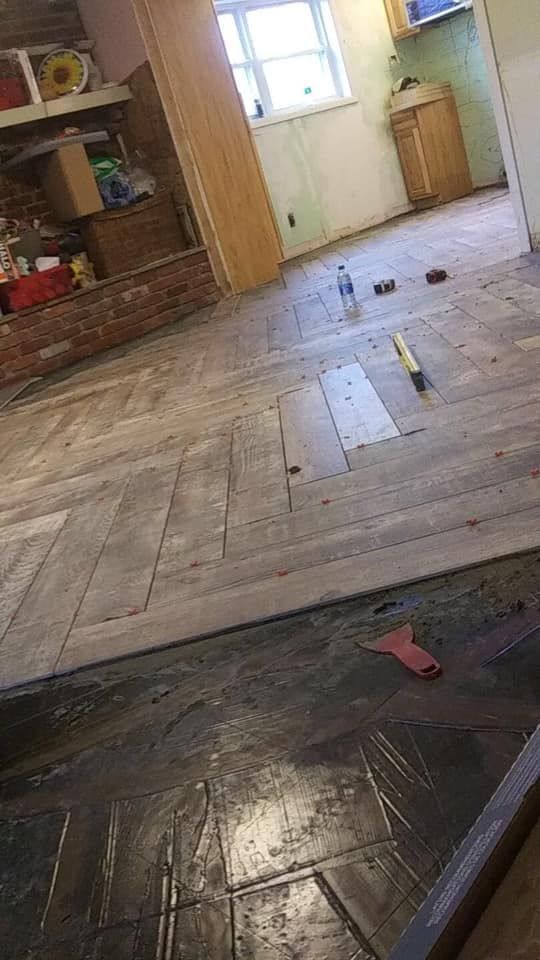 Wood floors being renovated in a kitchen; old tile in the foreground; a window in the background.