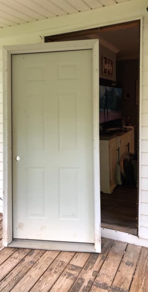 White door on wooden porch, slightly ajar, opening into a room with a TV and cabinets.