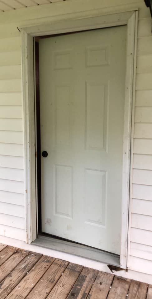 White door with six panels, set in white frame, on a wooden porch.