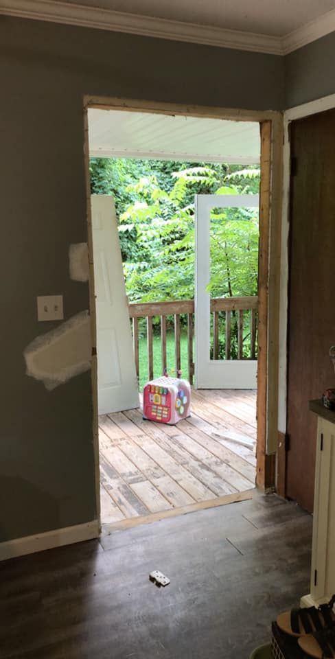 Doorway leading to a deck with a forested view. Construction materials are visible.