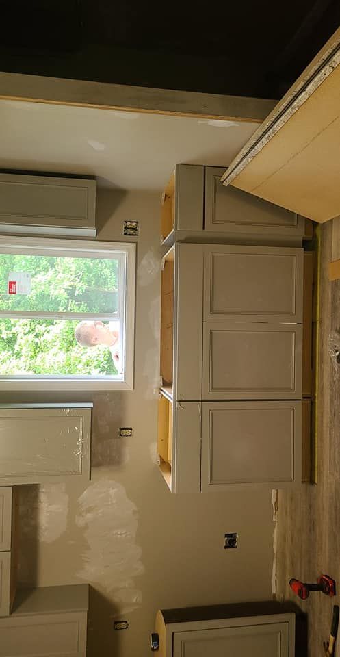 Kitchen cabinets in various positions, painted light gray, installed on a wall near a window.