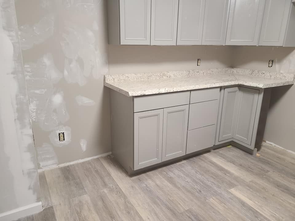 Gray kitchen cabinets with countertop, gray walls, and wood-look flooring.