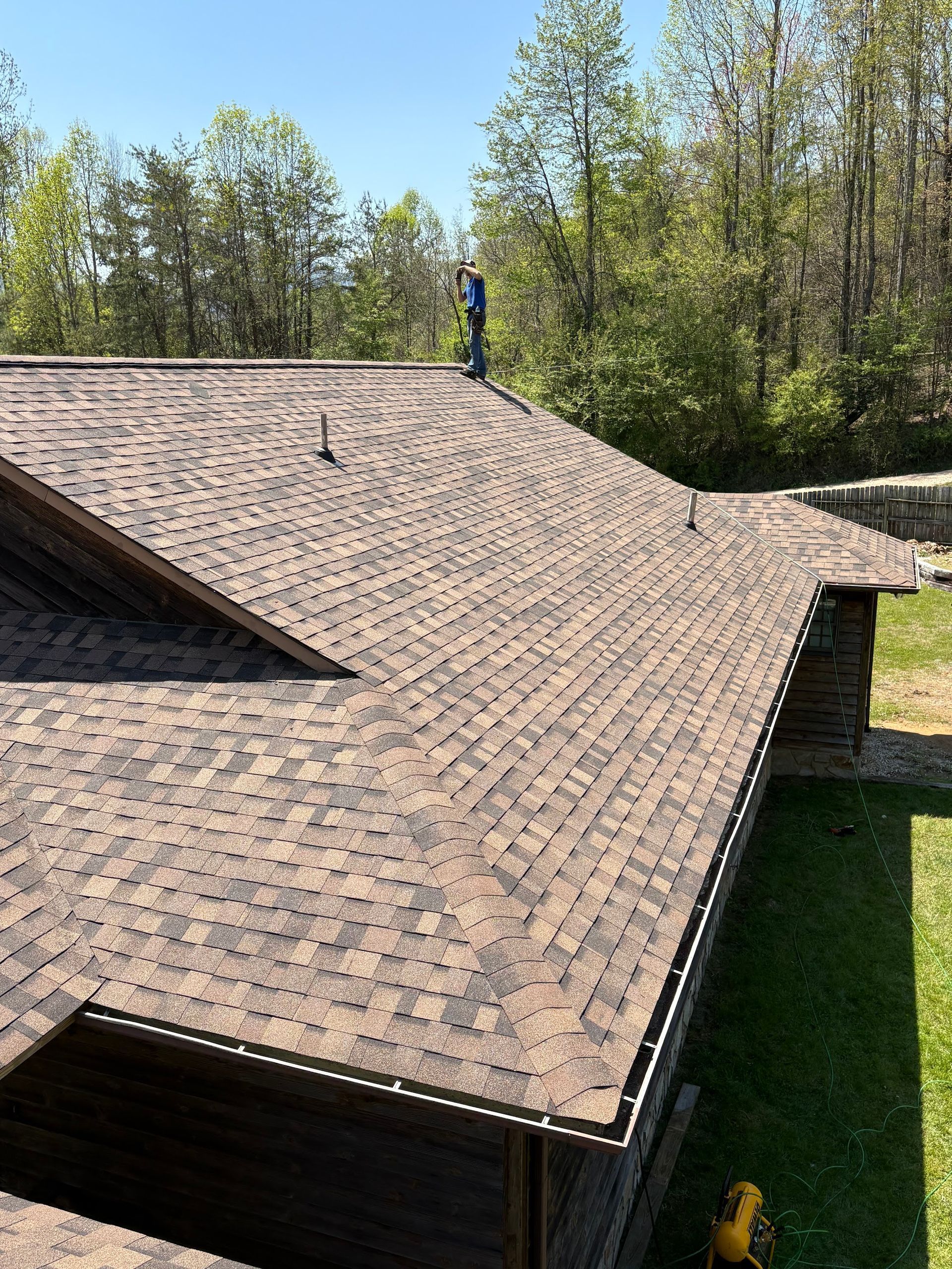 Brown shingle roof on a wooden building, person standing on it, sunny day.