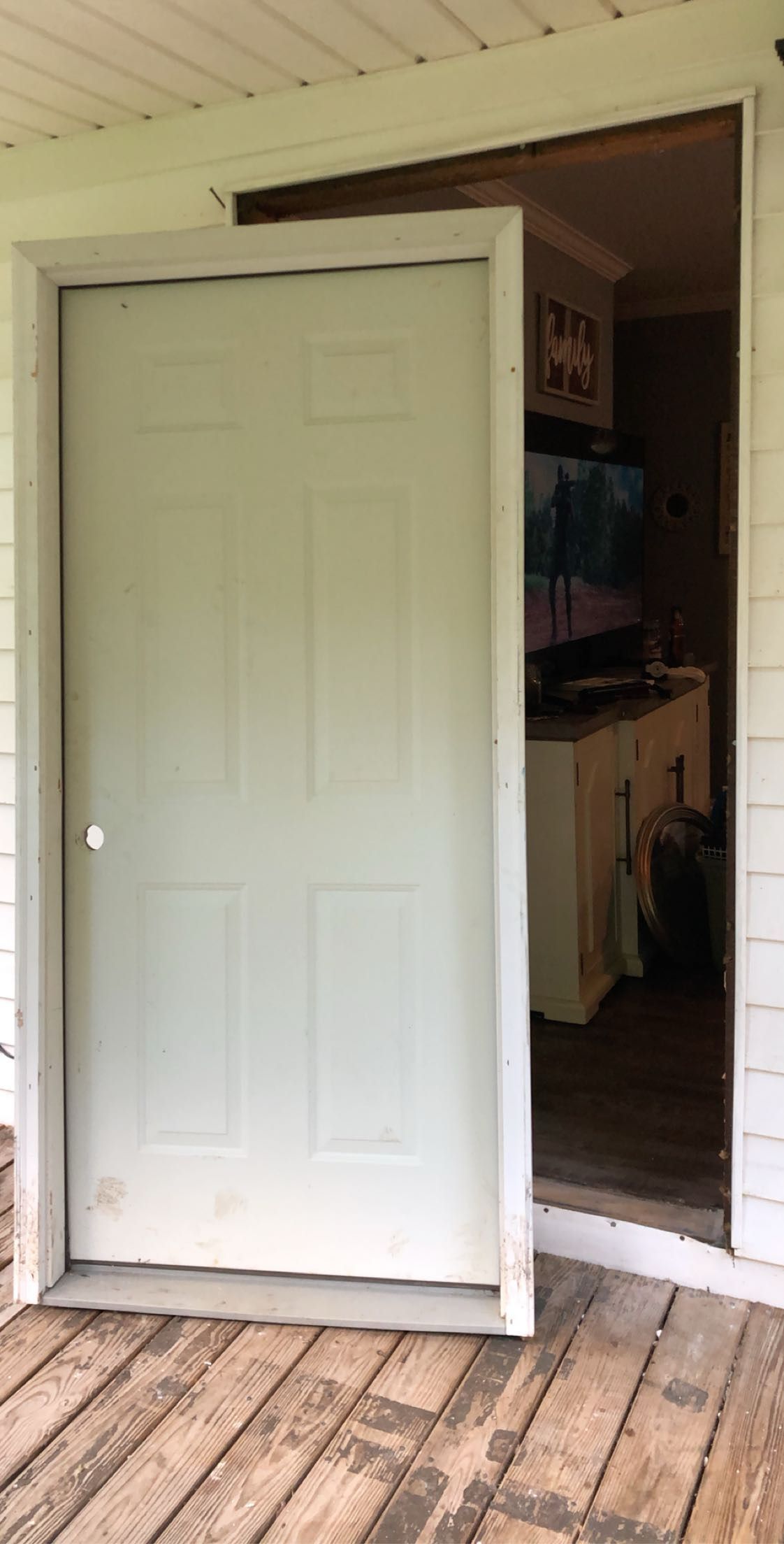 White door on a wooden porch, slightly ajar, revealing interior with TV and cabinet.