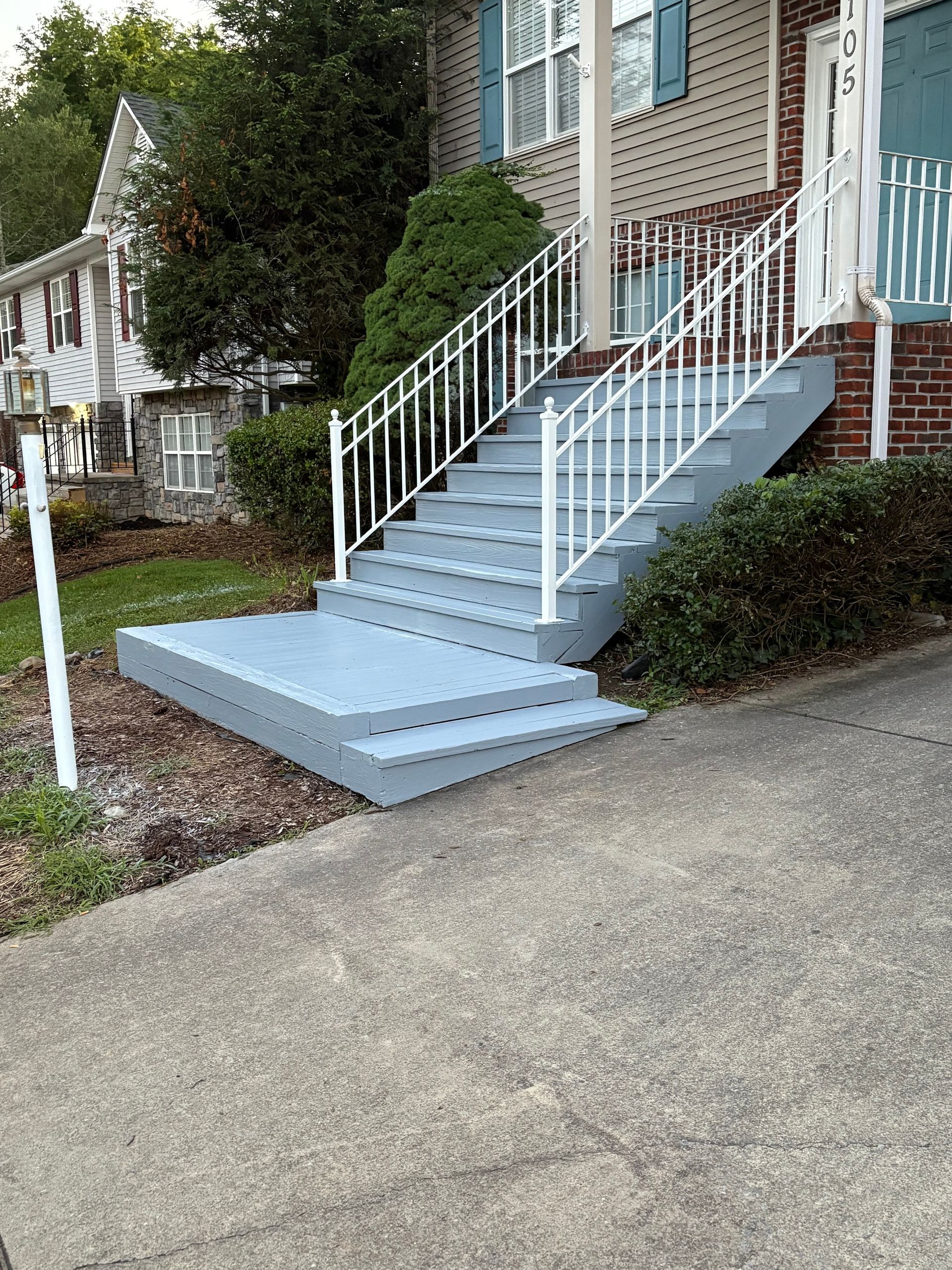 Gray painted exterior stairs with white railing leading to a house, next to a concrete sidewalk.