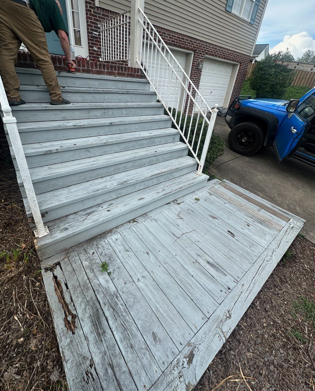 Exterior view of gray wooden stairs and landing. A person stands on the stairs near a white railing.