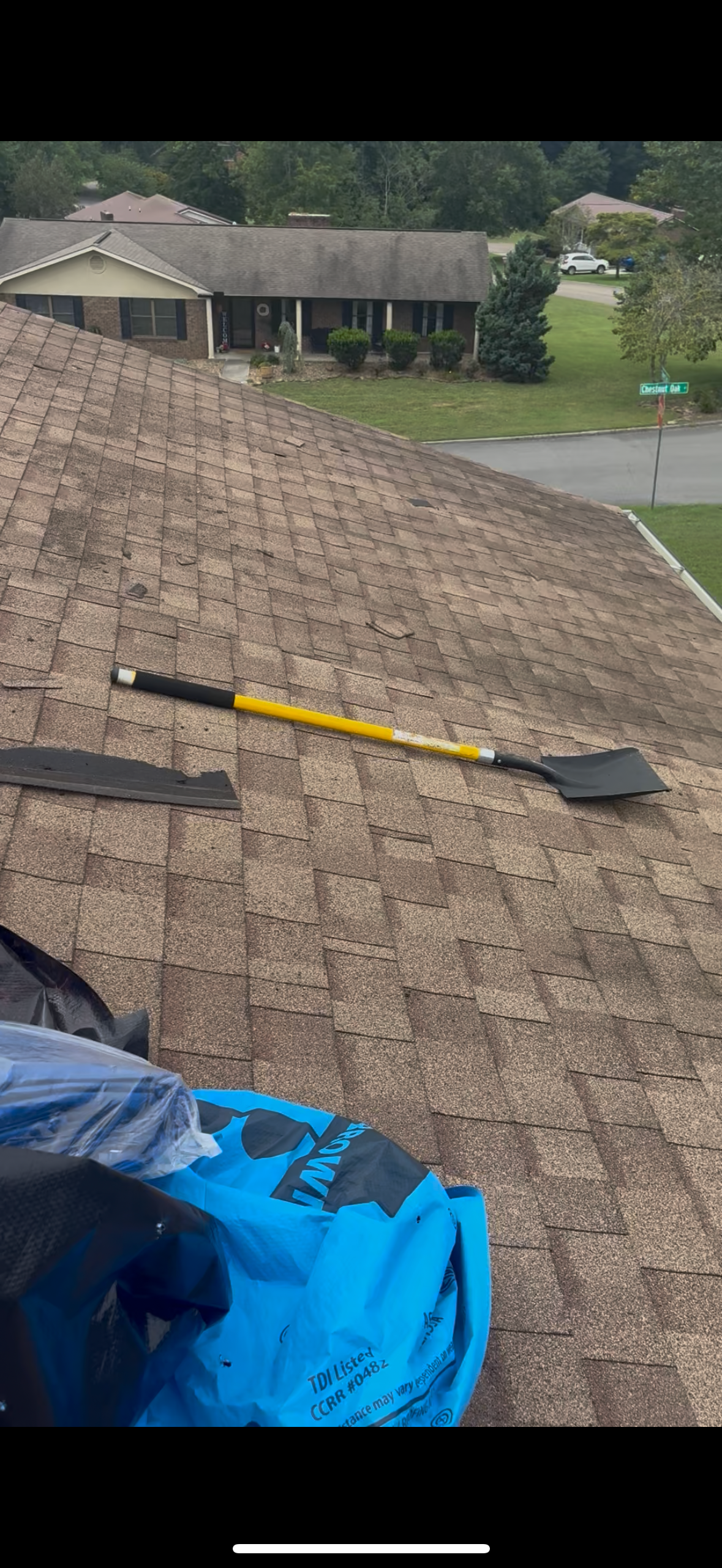 Roofer's tools on a roof with a residential home in the background. Blue tarp is visible.