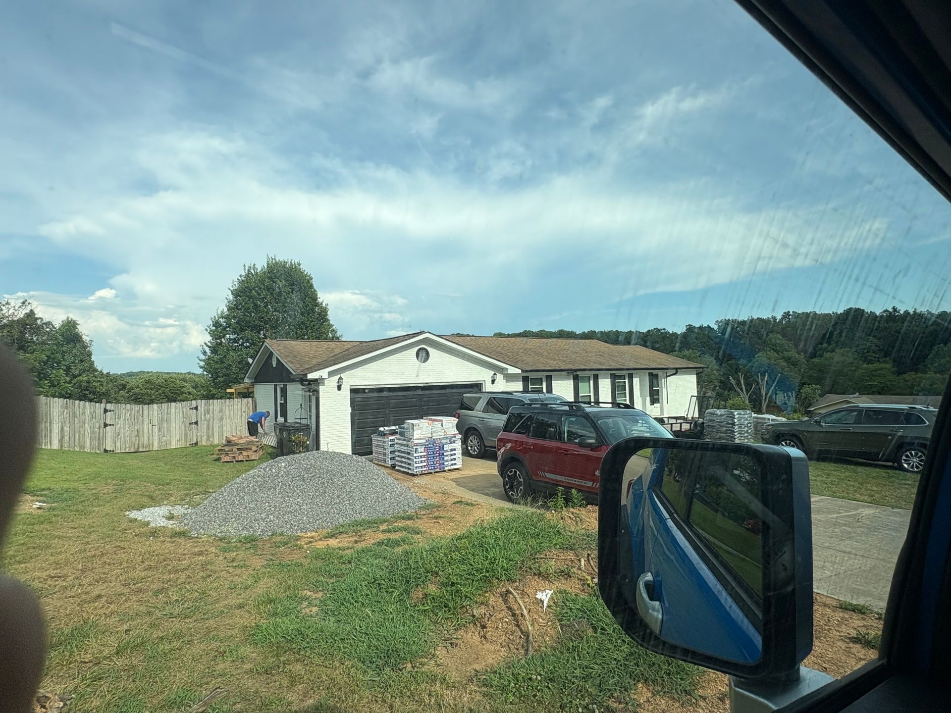 A single-story house with construction materials and vehicles in front under a cloudy sky.