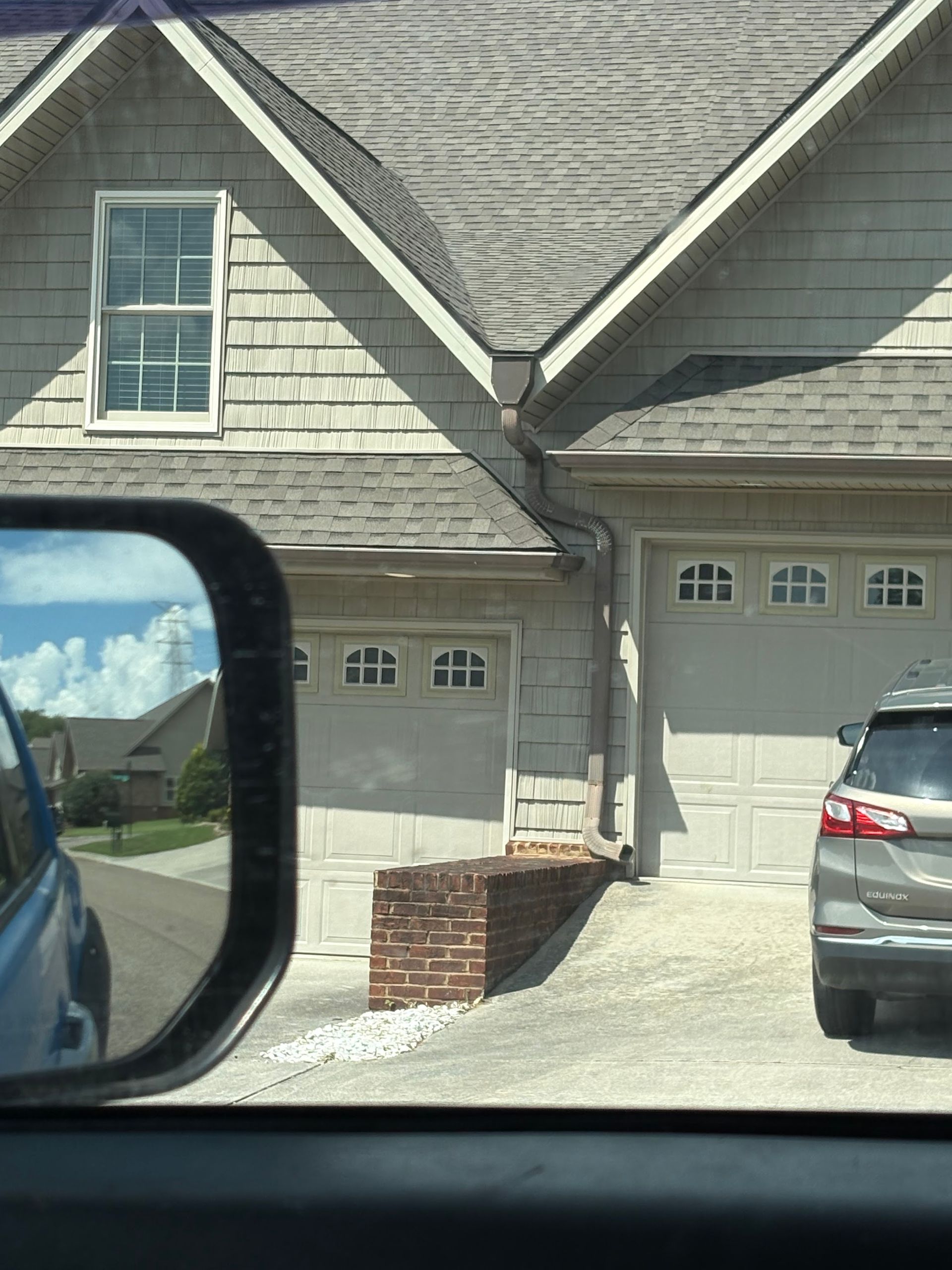 Two-car garage with brick retaining wall. A car is parked in the right garage. Reflection in side mirror.