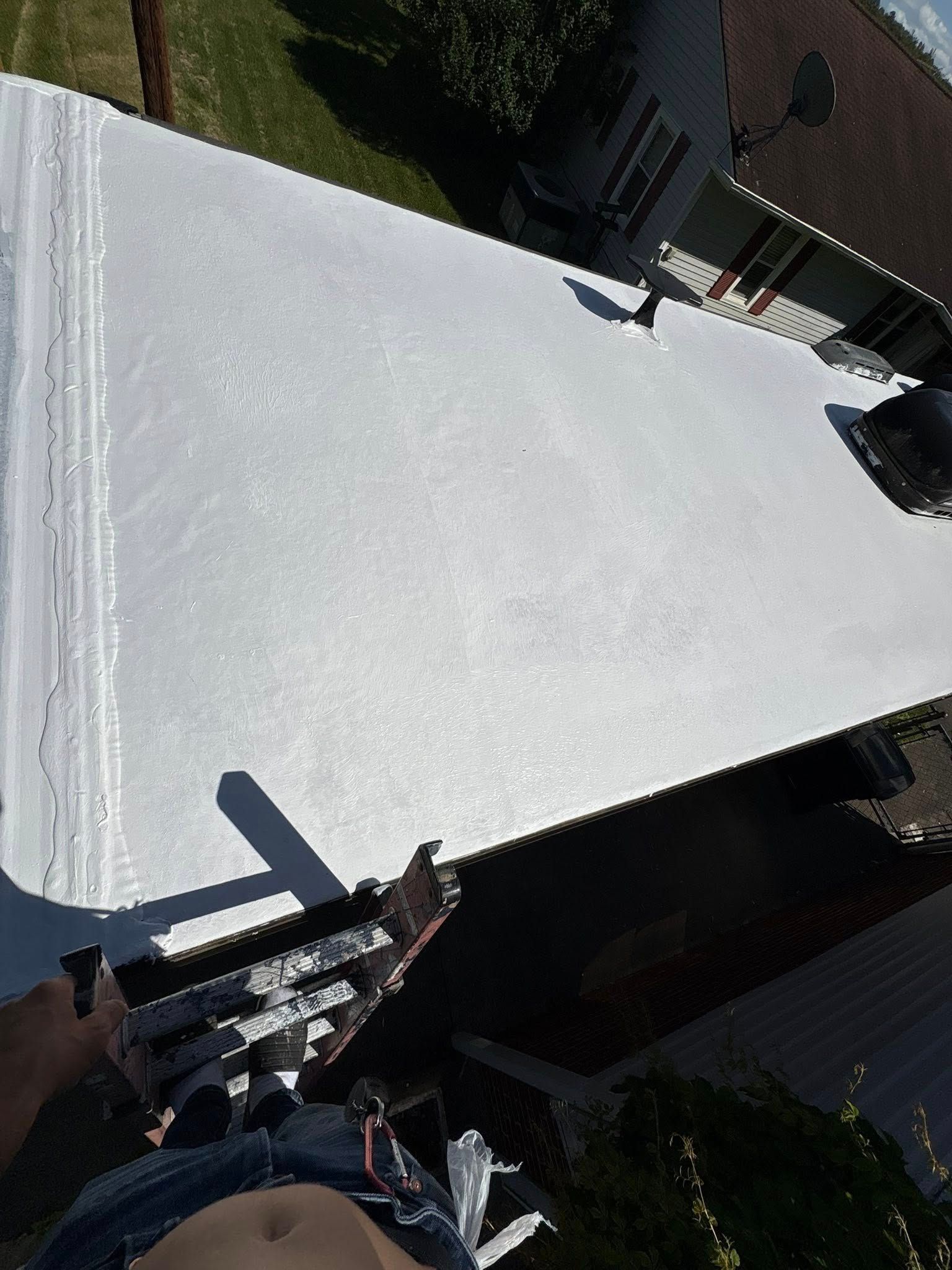 Person on ladder looking at white roof; residential setting.