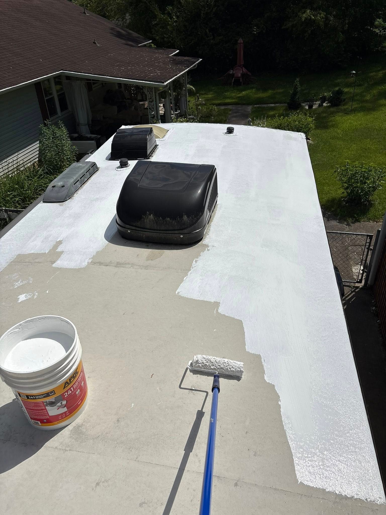 A person using a paint roller to apply white sealant on a flat RV roof.