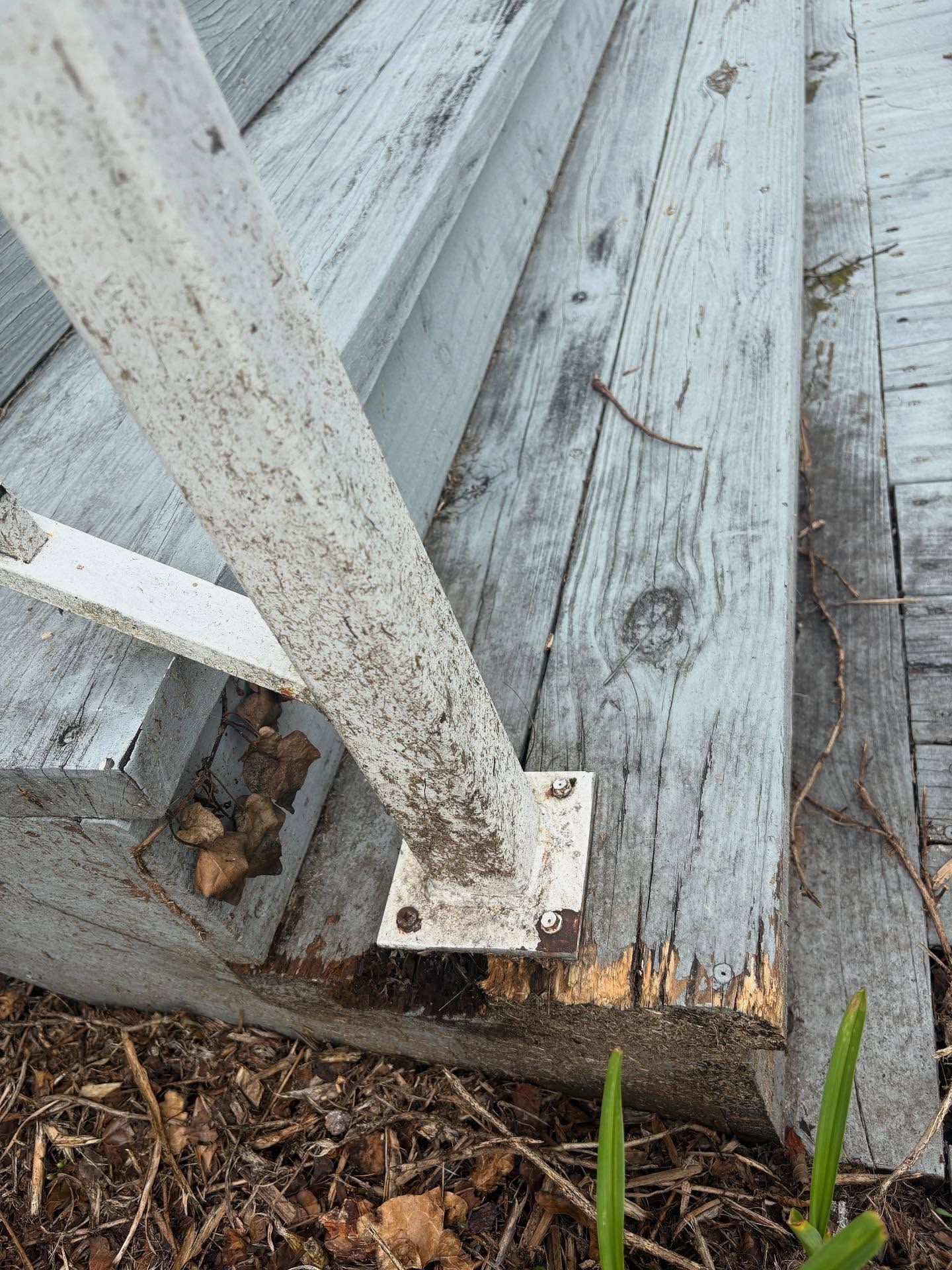 Close-up of weathered, painted wooden porch with a white metal railing. Some debris is visible on the wood and ground.