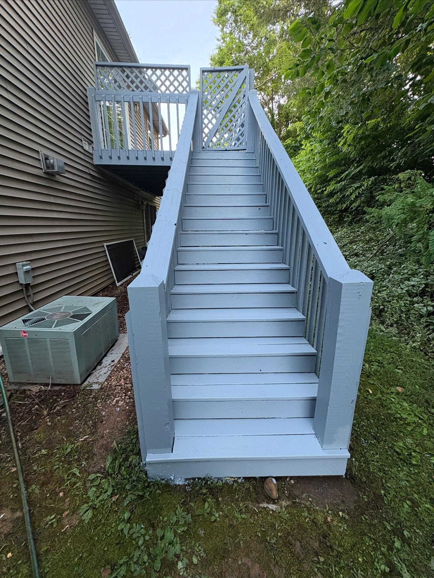 Gray painted wooden staircase leading up to a deck attached to a house; outdoor setting.
