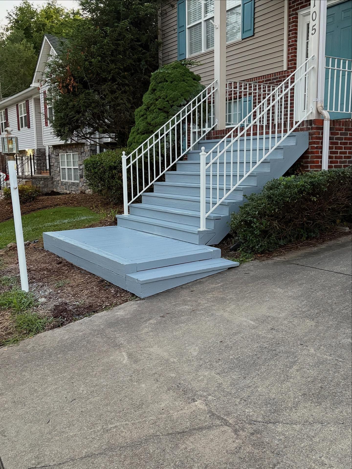 Blue painted exterior stairs with white railing leading to a brick house entrance.