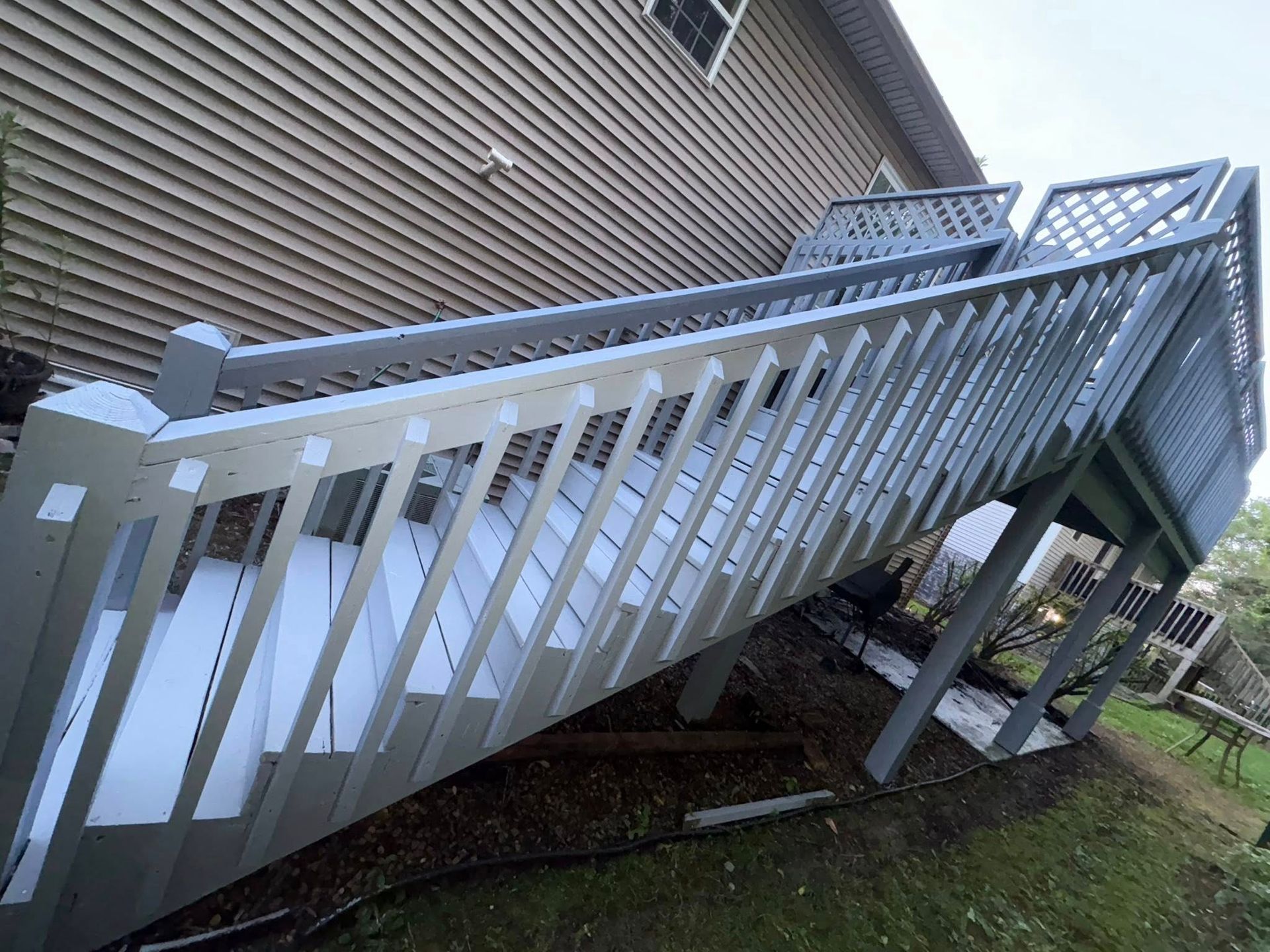 A gray painted wooden deck with railings. Sloping stairs lead down to a grassy yard.