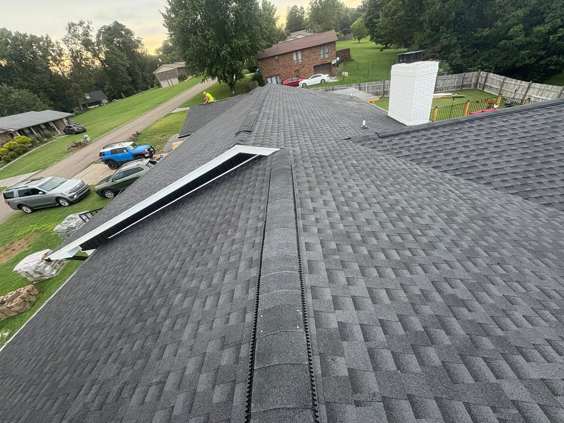 Dark gray shingled roof, valley and chimney with metal flashing, residential setting.